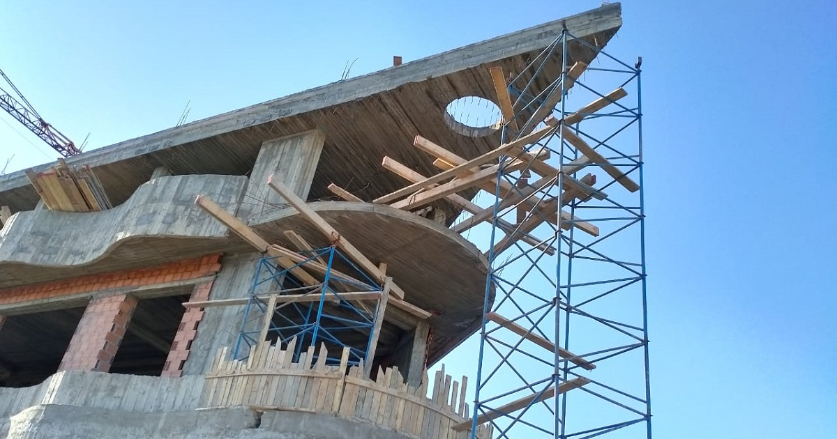 Workers on blue scaffolding removing wooden formwork and shores from underneath a newly cast concrete post tension slab on a construction site.